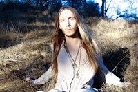 a man with long hair sitting in a field